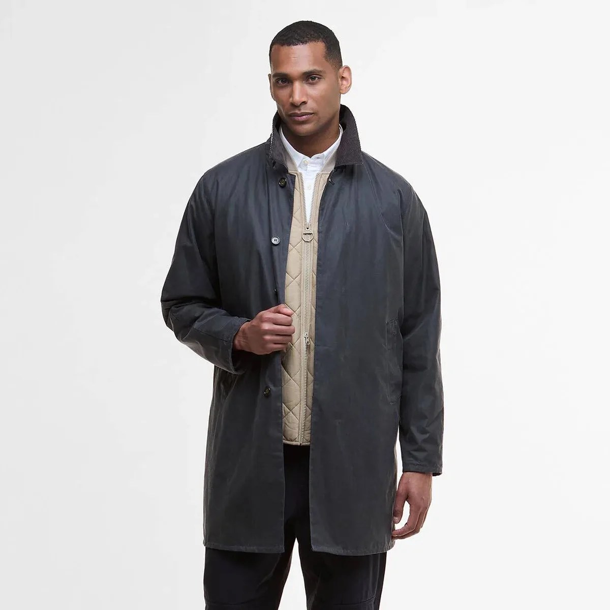 Man wearing a dark gray buttoned coat over a beige quilted zip-up jacket and white shirt.