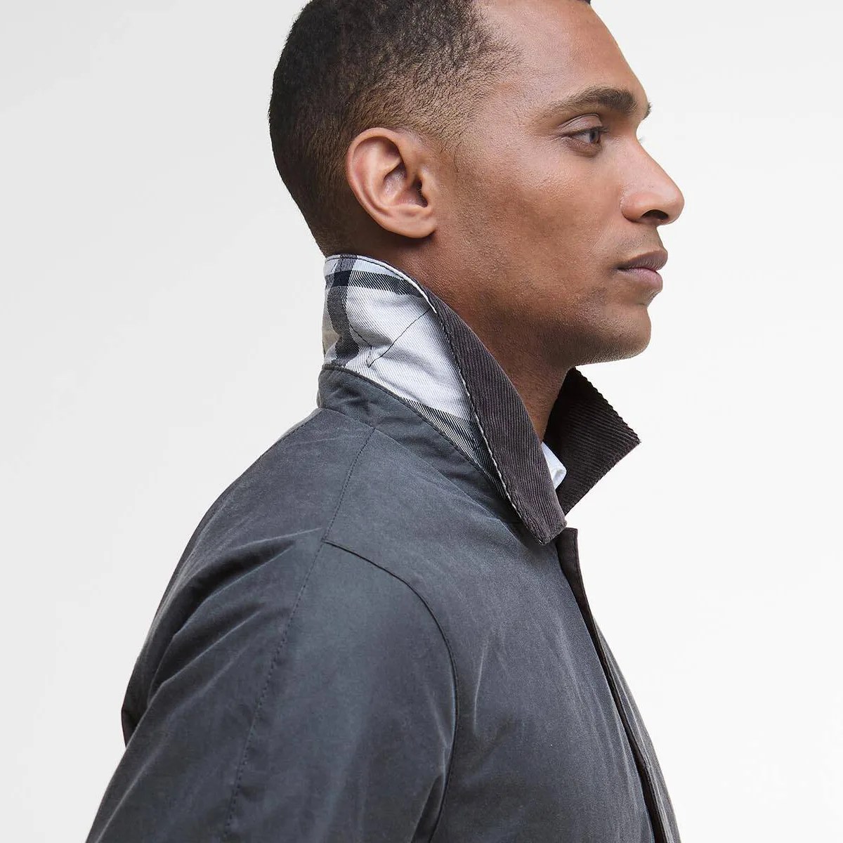 Side profile of a person wearing a dark gray jacket with a raised collar showing a black and white checkered inner lining.