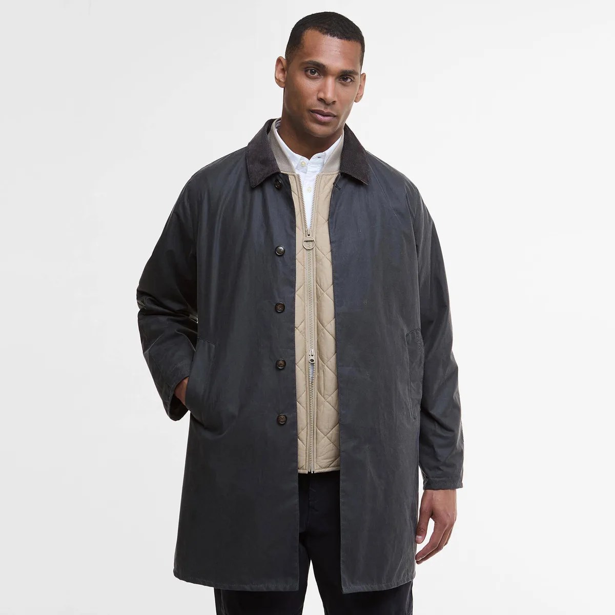 Man wearing a dark gray button-up coat with a black collar over a beige quilted zip-up jacket.