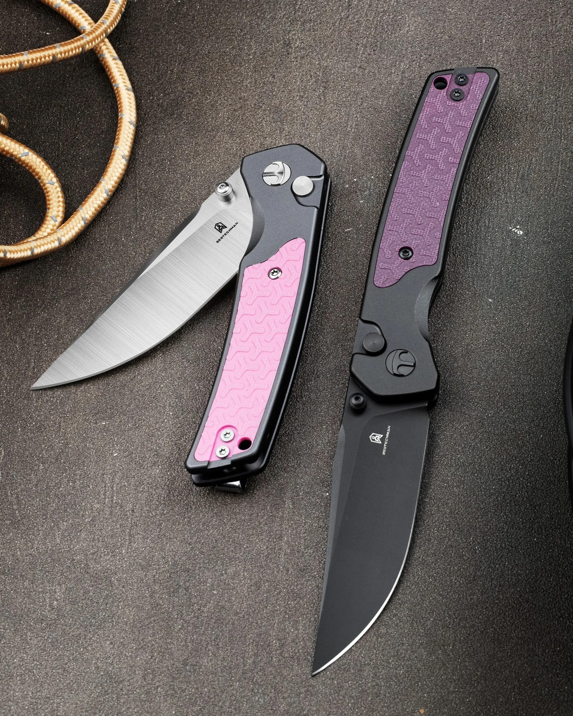 Two folding knives with textured pink and purple handles, one with a silver blade open and the other with a black blade closed, on a dark surface.