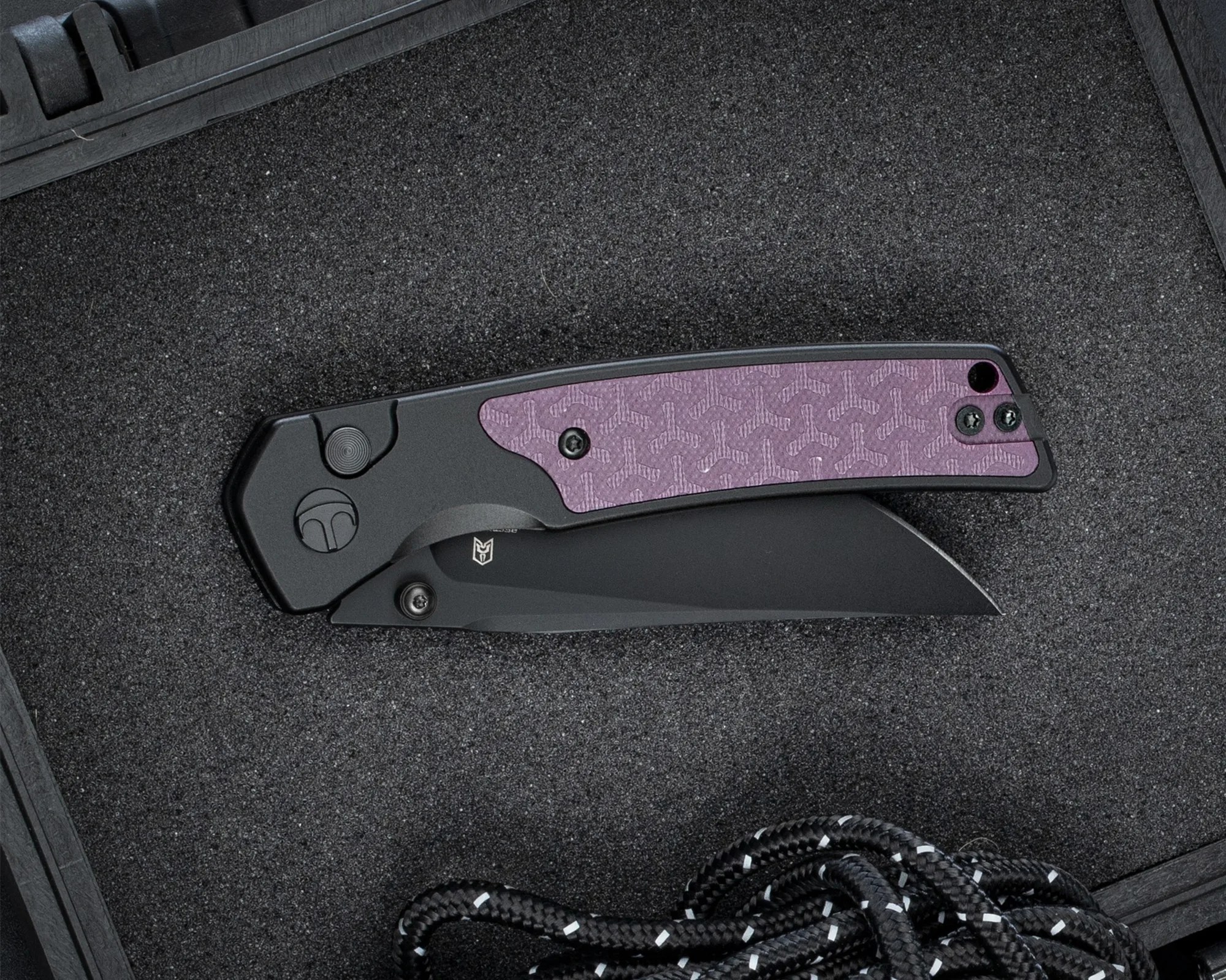 Black folding knife with a purple textured handle panel resting on black foam inside a case.