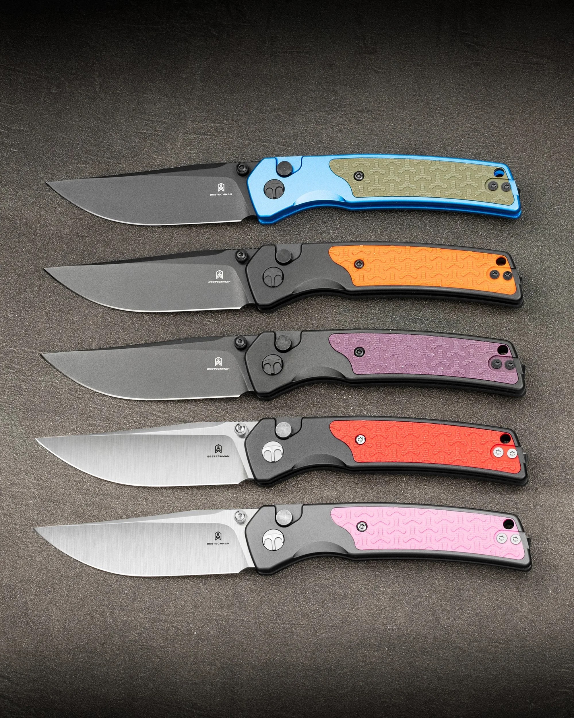 Five folding knives with different colored handles (blue, orange, purple, red, pink) and Bestechman logos on the blades, arranged in a row on a dark surface.