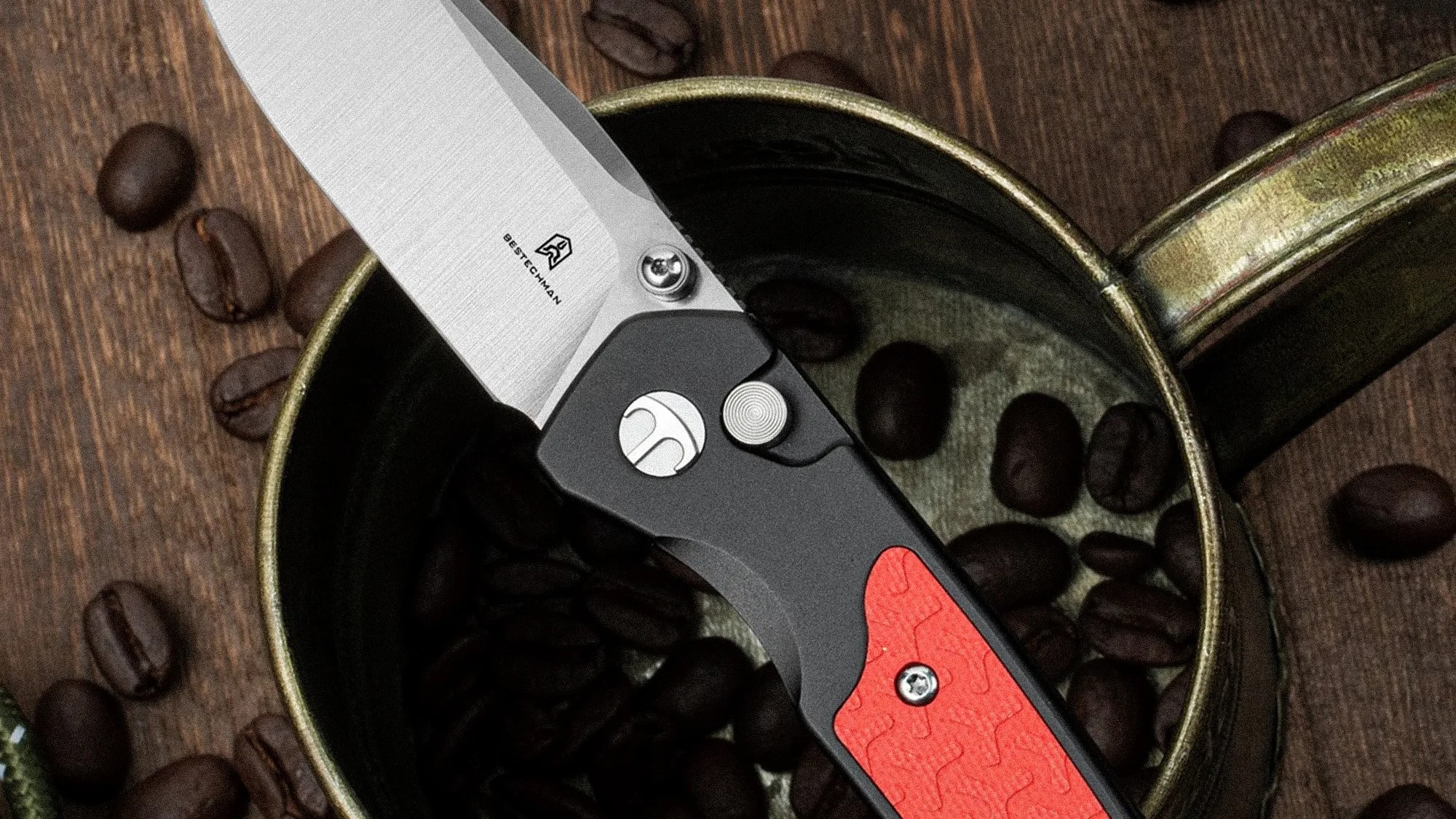 Folding knife with a silver blade and black handle featuring a red textured grip, resting in a cup with coffee beans.