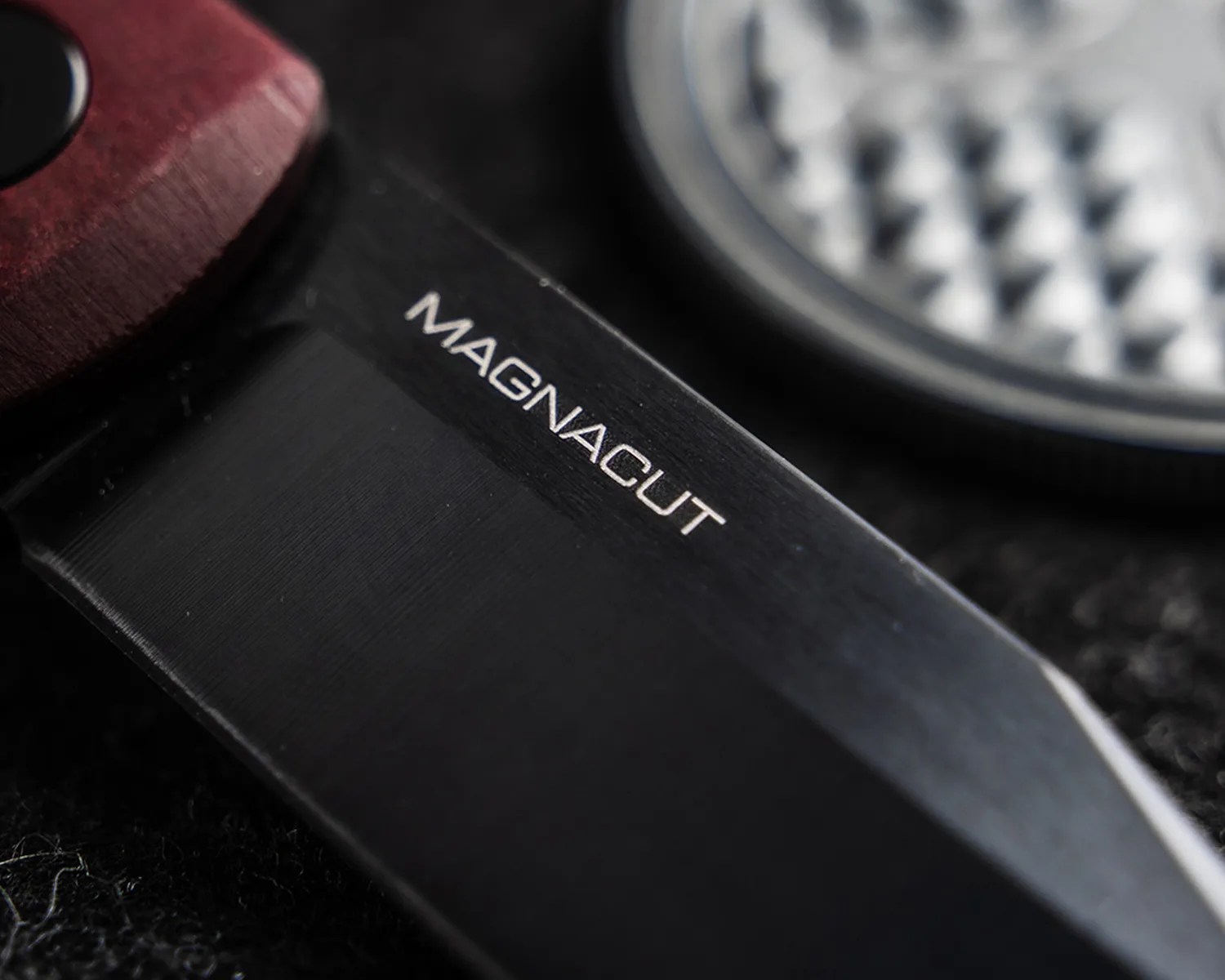 Close-up of a black knife blade with the word "MAGNACUT" engraved near a wooden handle.