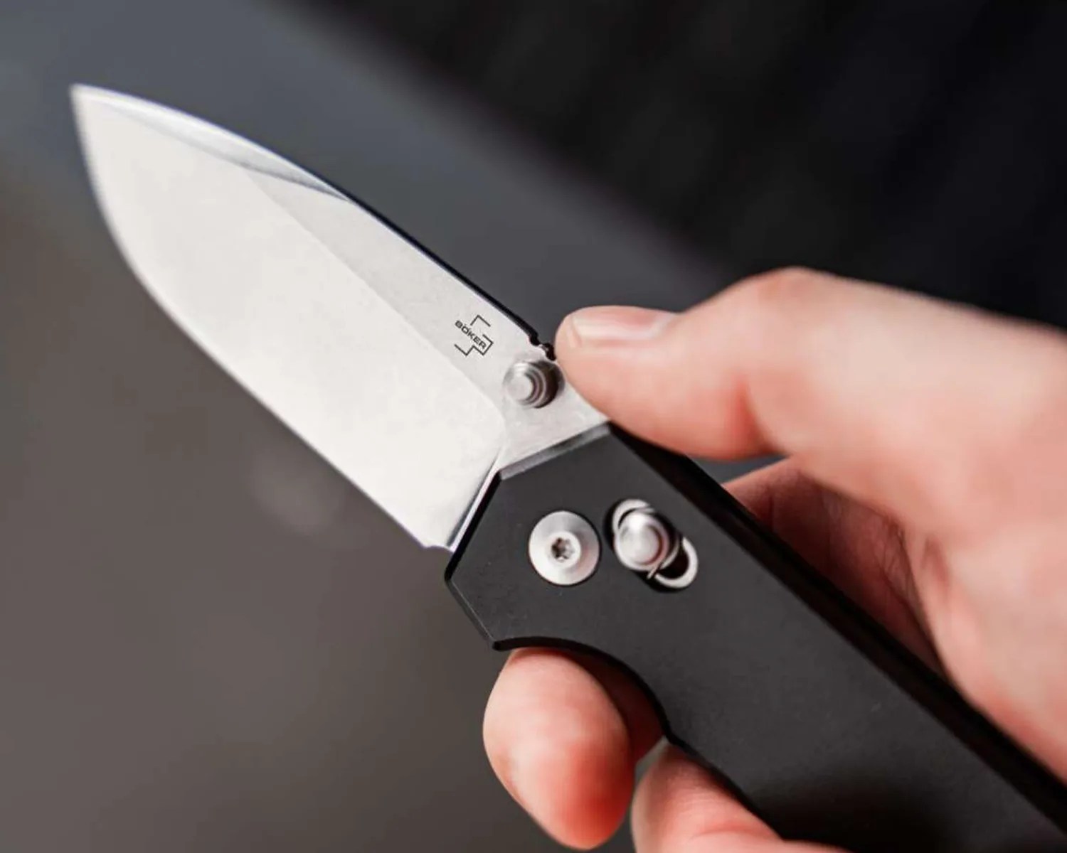 Hand holding a folding knife with a silver blade and black handle, showing the Boker logo on the blade.