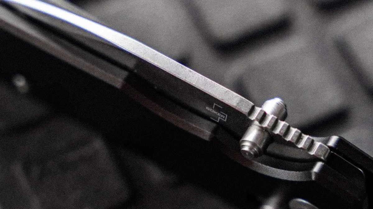 Close-up of a folding knife's locking mechanism and blade spine with a textured metal surface.