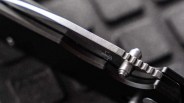 Close-up of a folding knife's locking mechanism and blade spine with a textured metal surface.