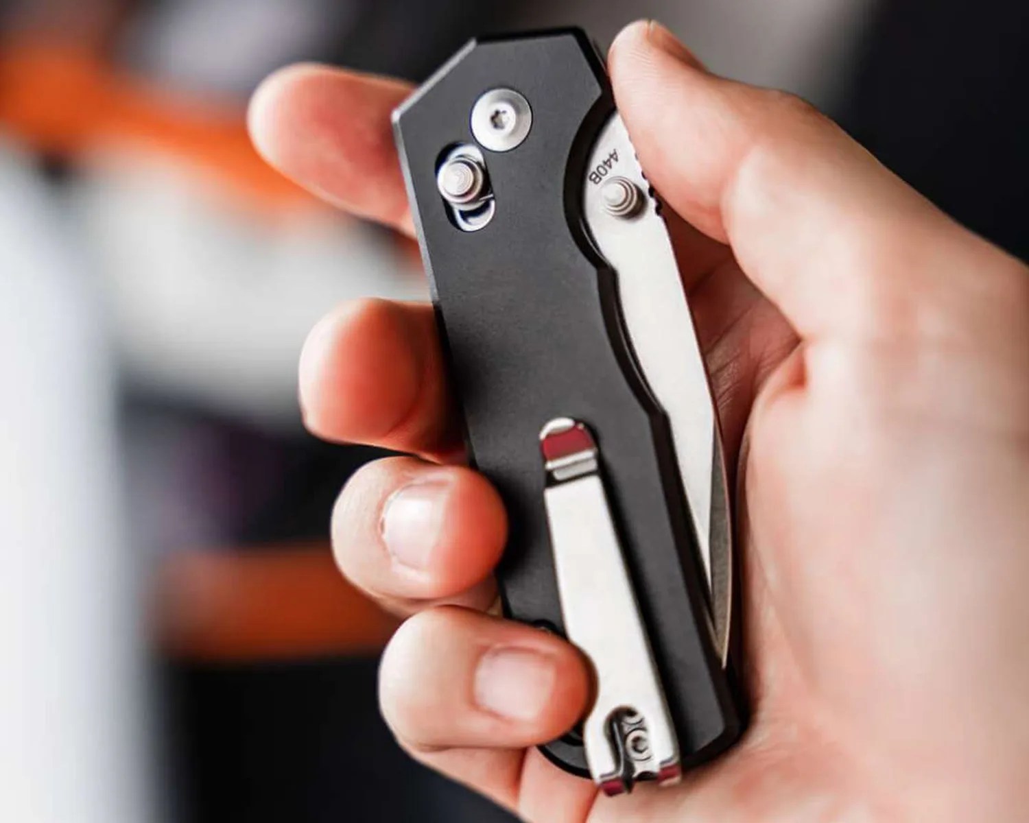 Hand holding a closed black folding pocket knife with a silver clip and visible screws.