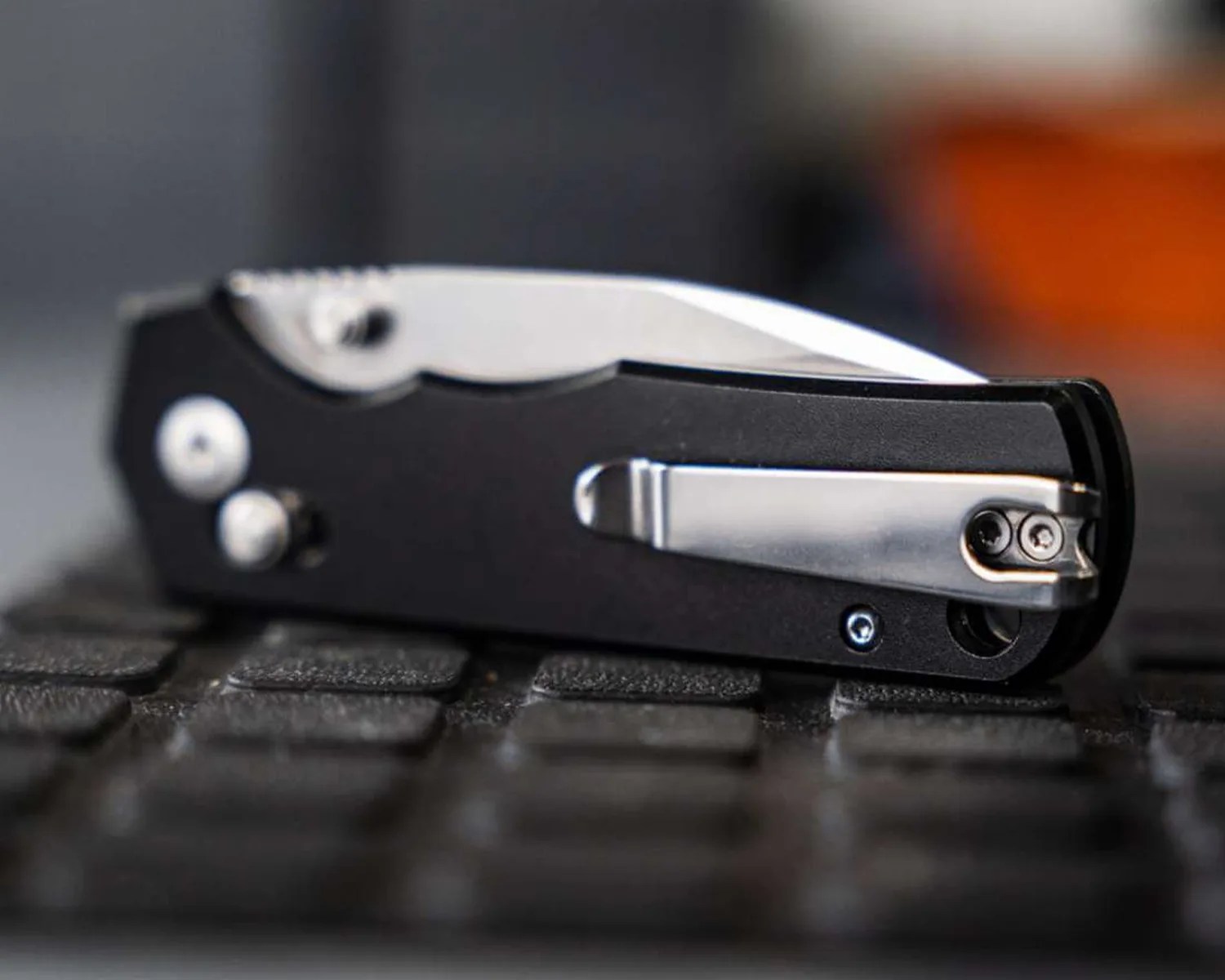 Black folding pocket knife with a partially visible silver blade and metal clip resting on a textured surface.