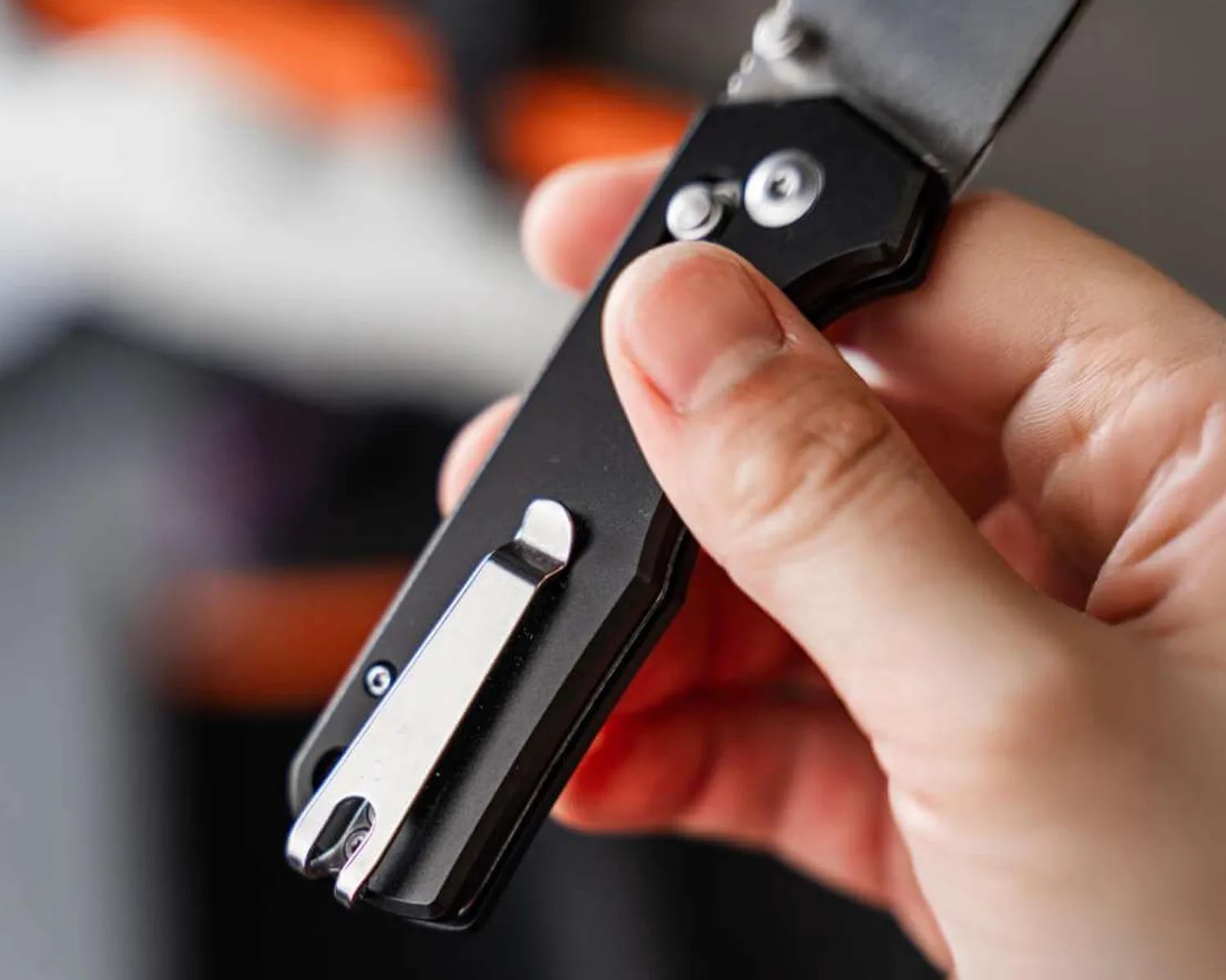 Hand holding a black folding knife with a silver pocket clip and thumb stud.