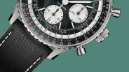 Close-up of a silver chronograph watch with black textured dial, white subdials, and black woven strap with white stitching.
