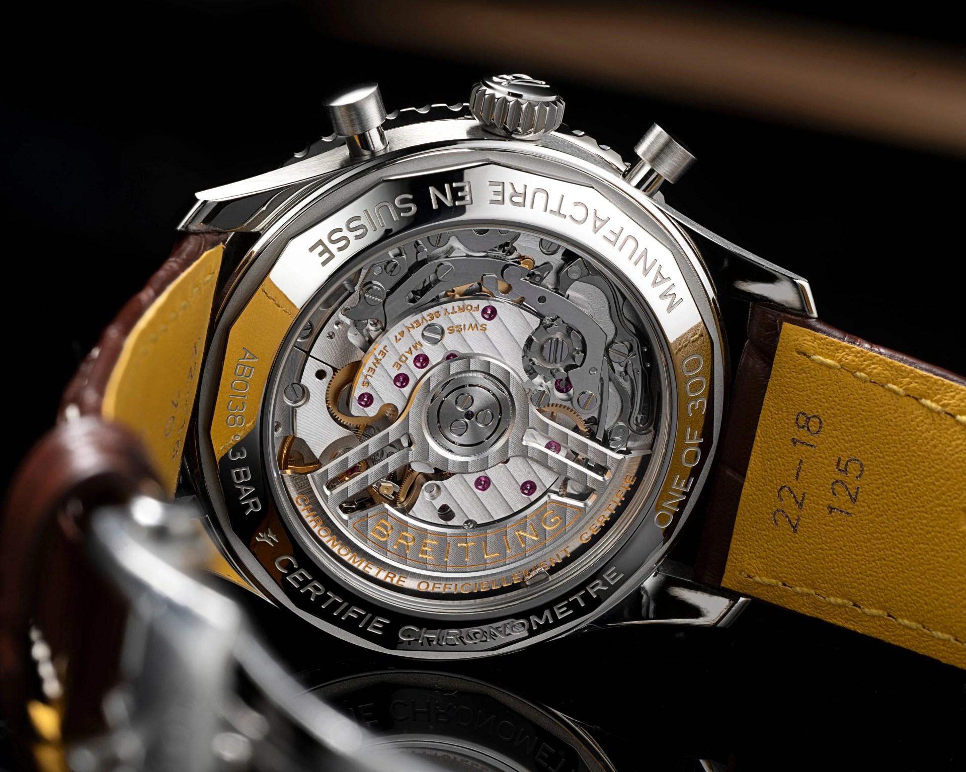 Close-up of the back of a Breitling watch showing the intricate mechanical movement through a transparent case back with a brown leather strap.