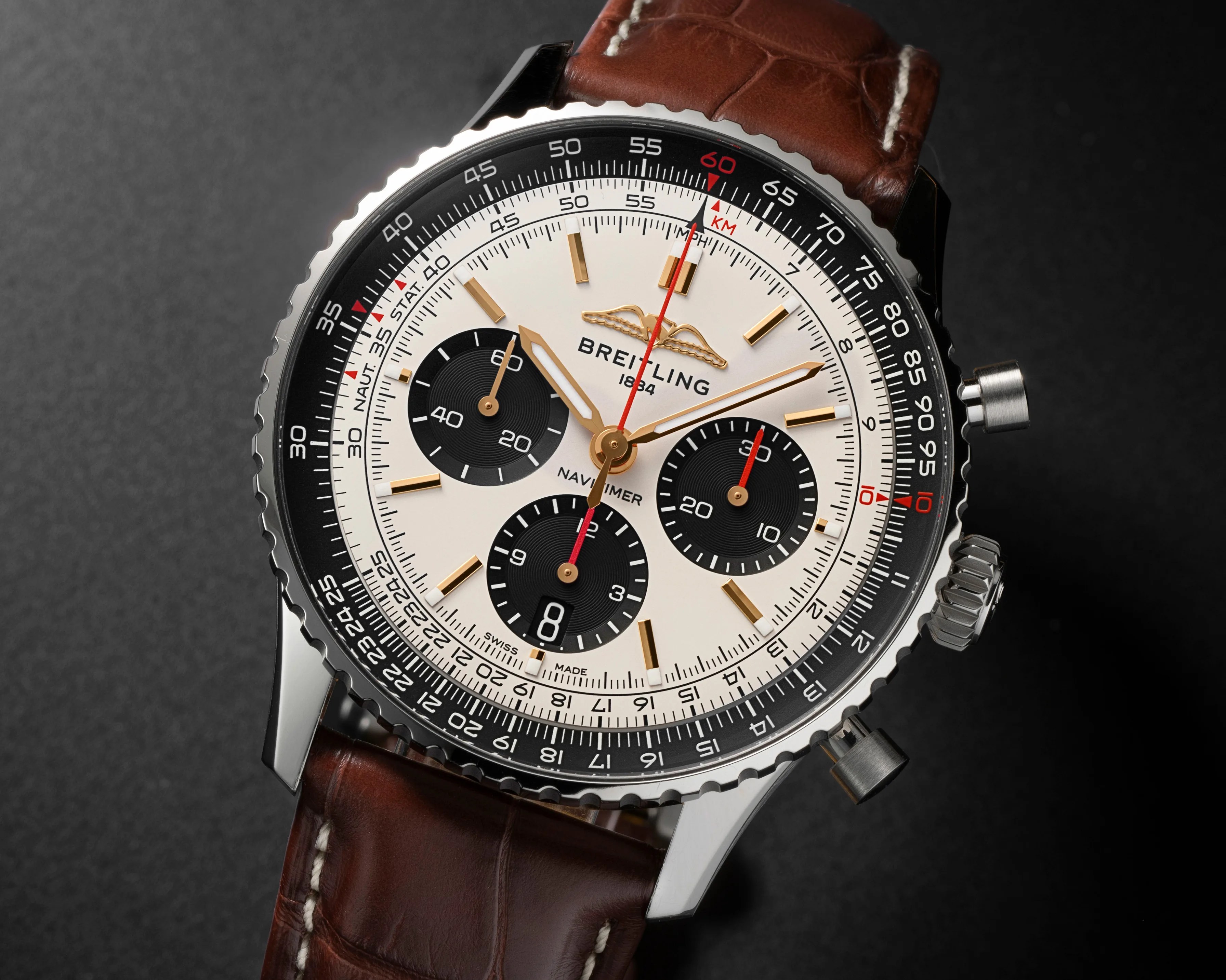 Breitling Navitimer watch with white dial, black subdials, gold markers, red second hand, and brown leather strap.