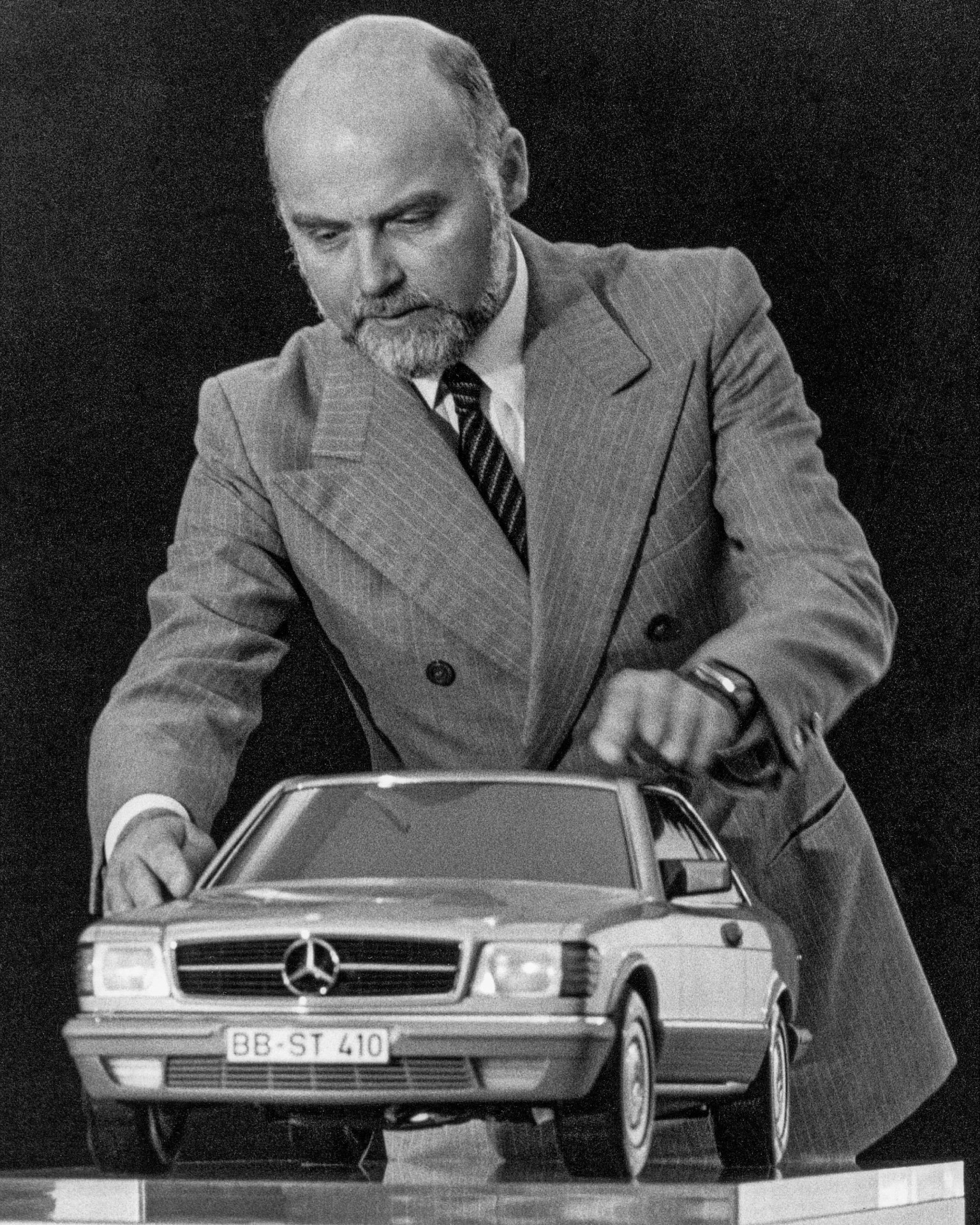 Man in a pinstripe suit adjusting a detailed scale model of a Mercedes-Benz car.