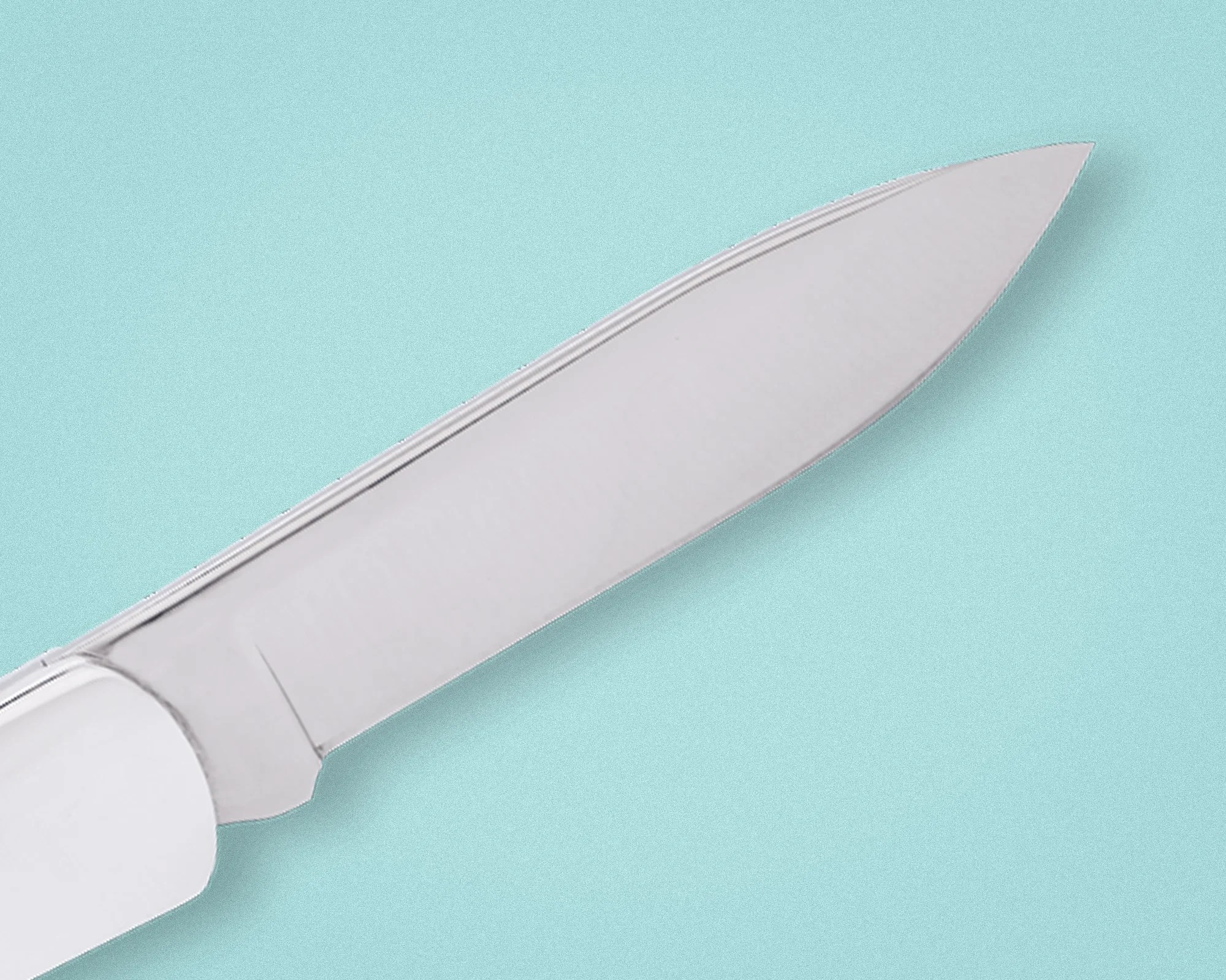 Close-up of a shiny stainless steel knife blade with a white handle on a light blue background.