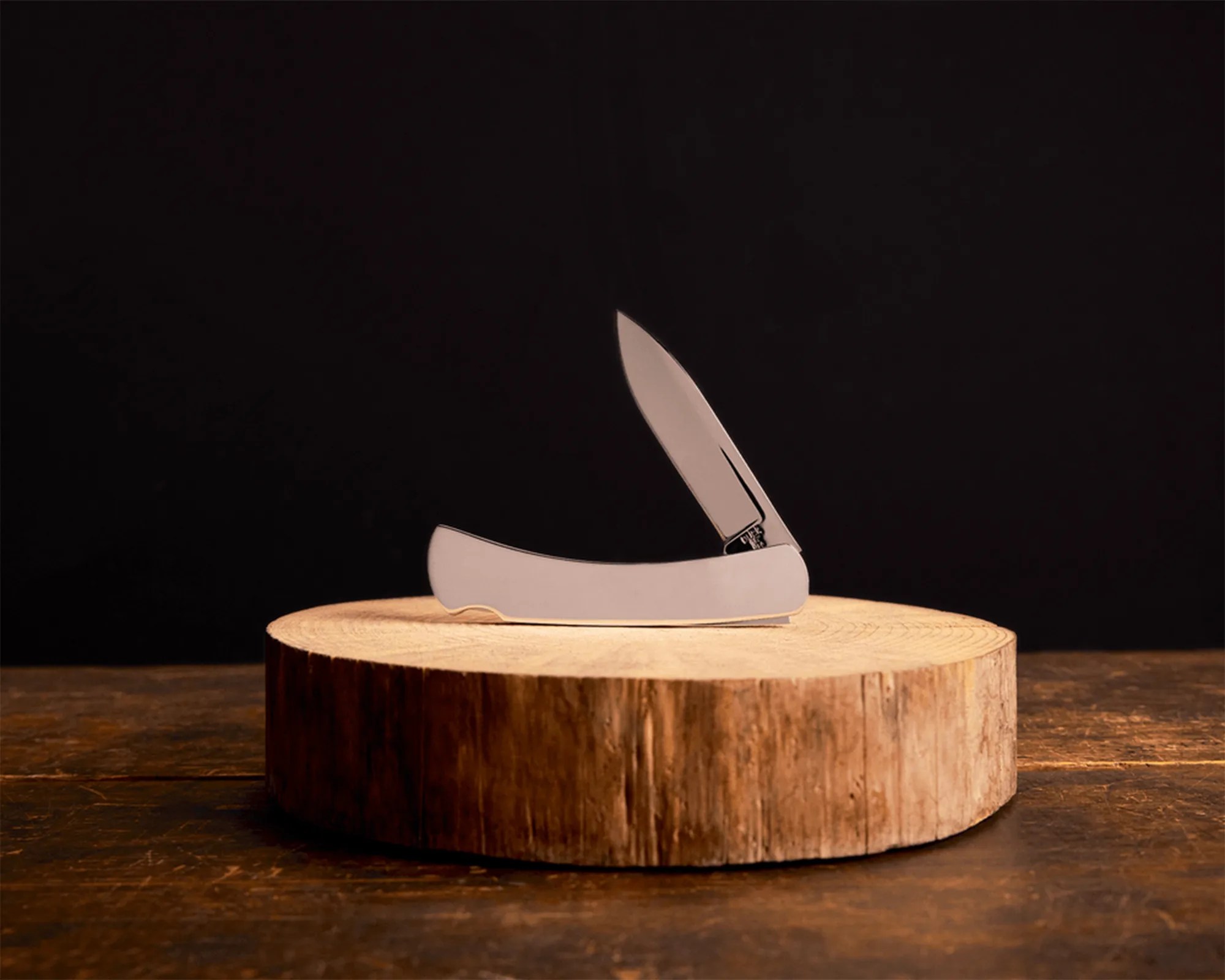 Silver folding pocket knife with one blade partially open on a round wooden block.