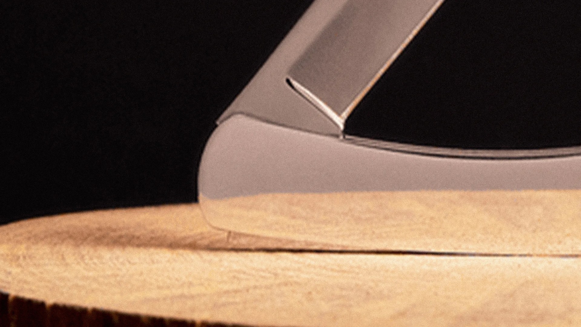 Close-up of a shiny metal knife blade resting on a wooden surface with a dark background.