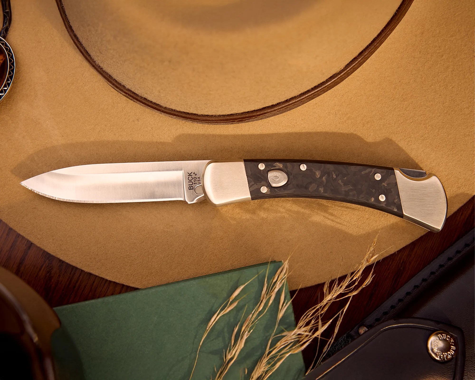 Buck 110 folding knife with a polished stainless steel blade and dark textured handle on a tan surface.