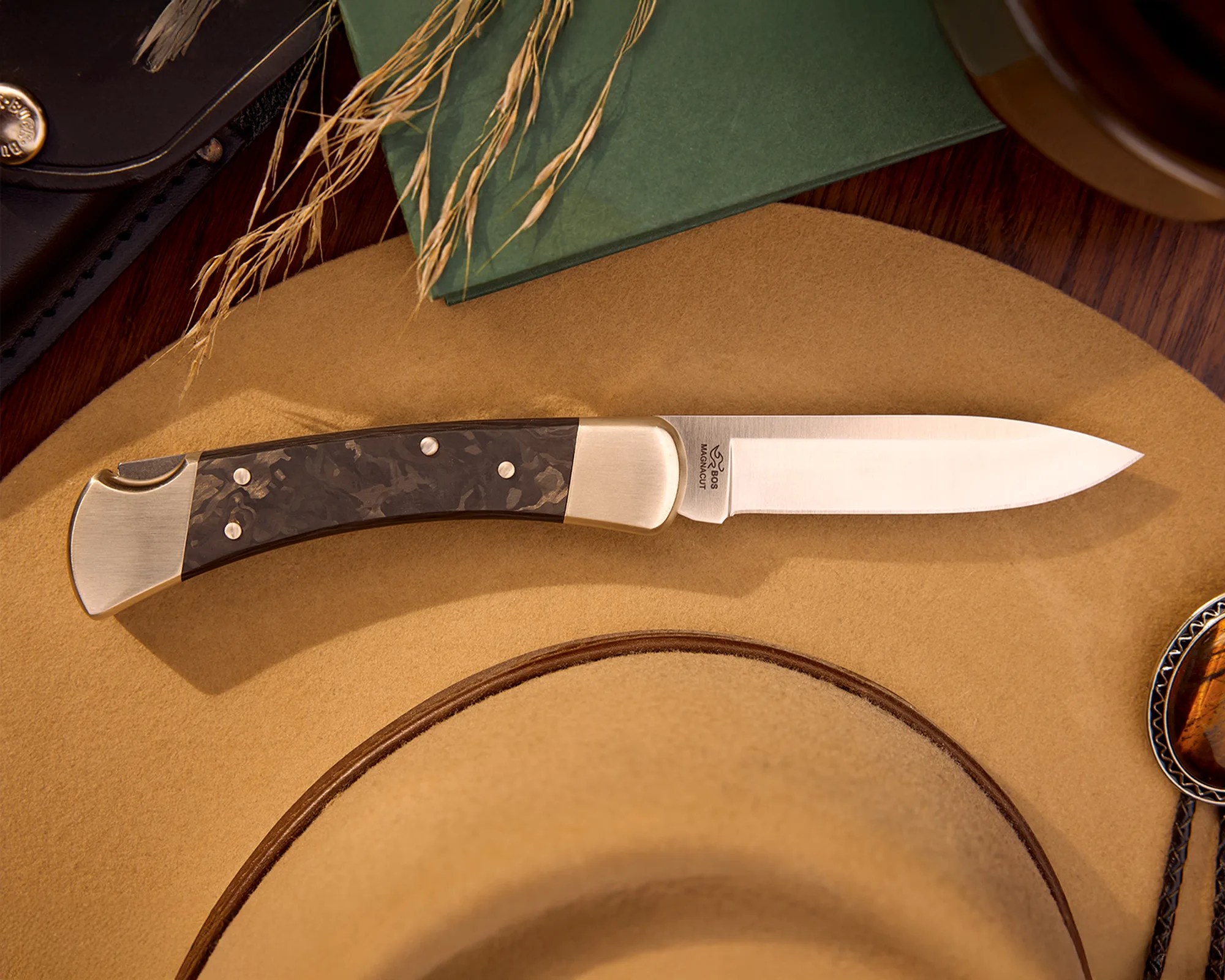 Folding pocket knife with a polished steel blade and dark marbled handle resting on a tan felt hat.