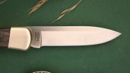 Knife blade with "BOS MAGNACUT" logo on a green background with dried grass.