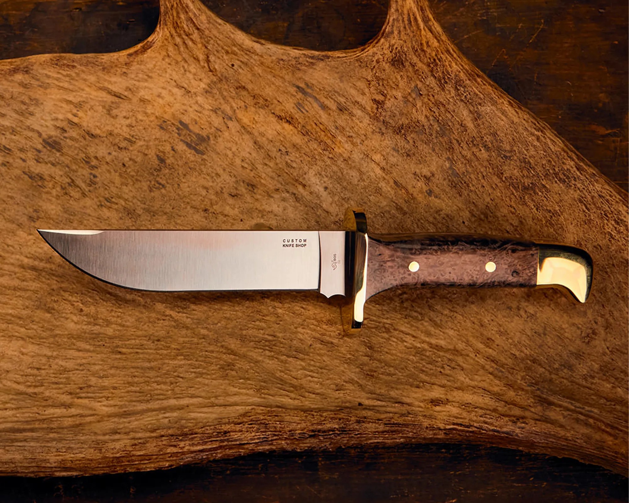 Fixed-blade knife with a polished steel blade, wooden handle, and brass guard and pommel on a wooden surface.