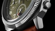 Close-up of a stainless steel watch case with a textured bezel, olive green dial, and brown leather strap.