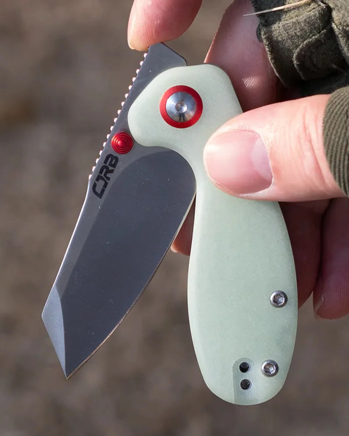 Compact folding knife with a gray blade and light green handle held in a hand.
