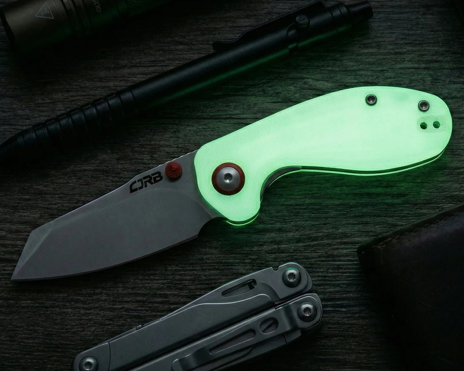Folding knife with a glowing green handle and a silver blade marked "CRB" on a dark wooden surface.