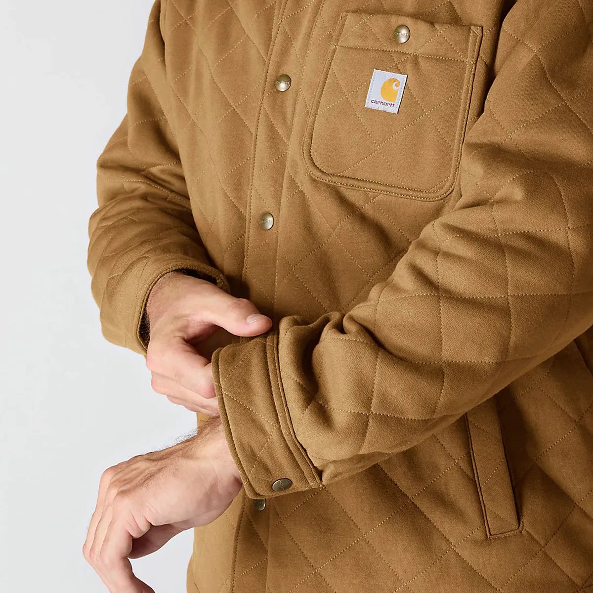 Brown quilted Carhartt jacket with snap buttons and chest pocket worn by a person adjusting the cuff.