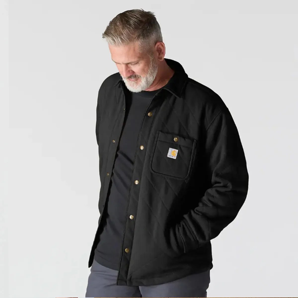 Man wearing a black quilted jacket with snap buttons and a chest pocket featuring a Carhartt logo patch.