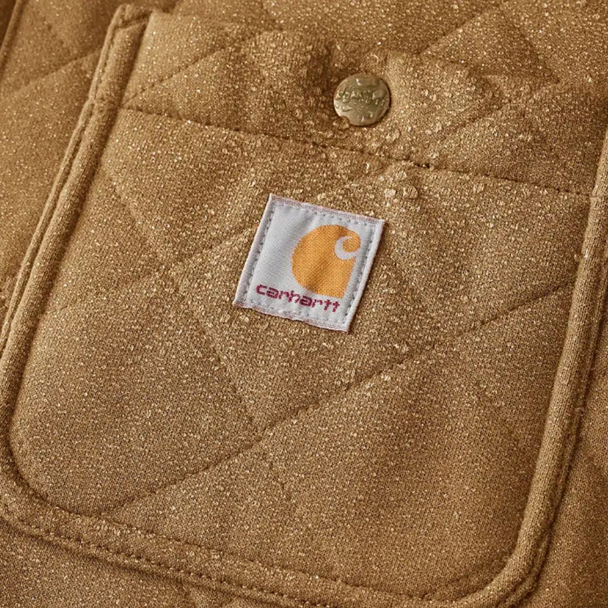 Close-up of a tan quilted Carhartt fabric with water droplets on the surface and a metal snap button.