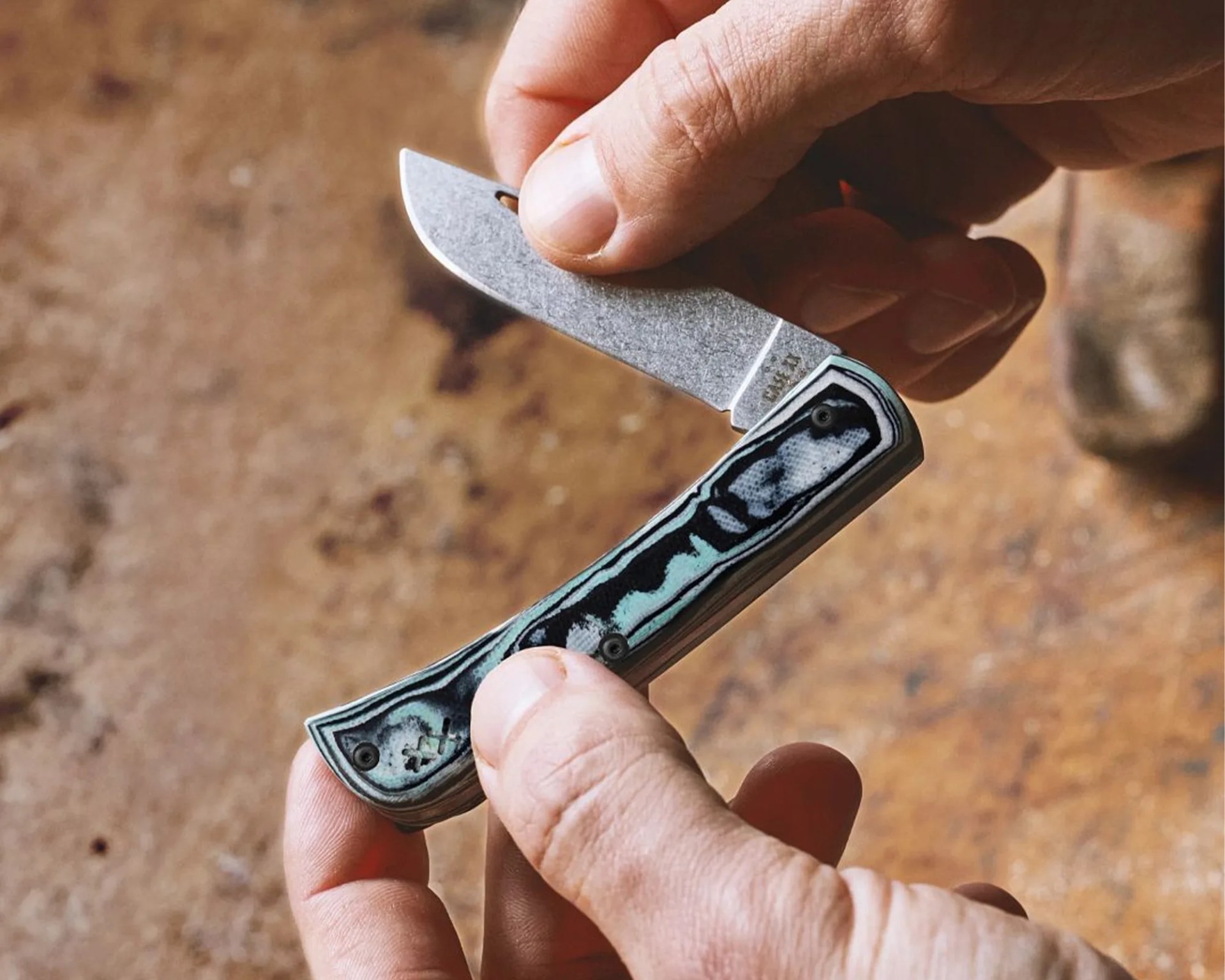 Small folding pocket knife with a stonewashed blade and a textured black and turquoise handle held in two hands.