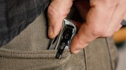 Hand placing a small folding knife with a black clip labeled "CASE" into a brown fabric pocket.