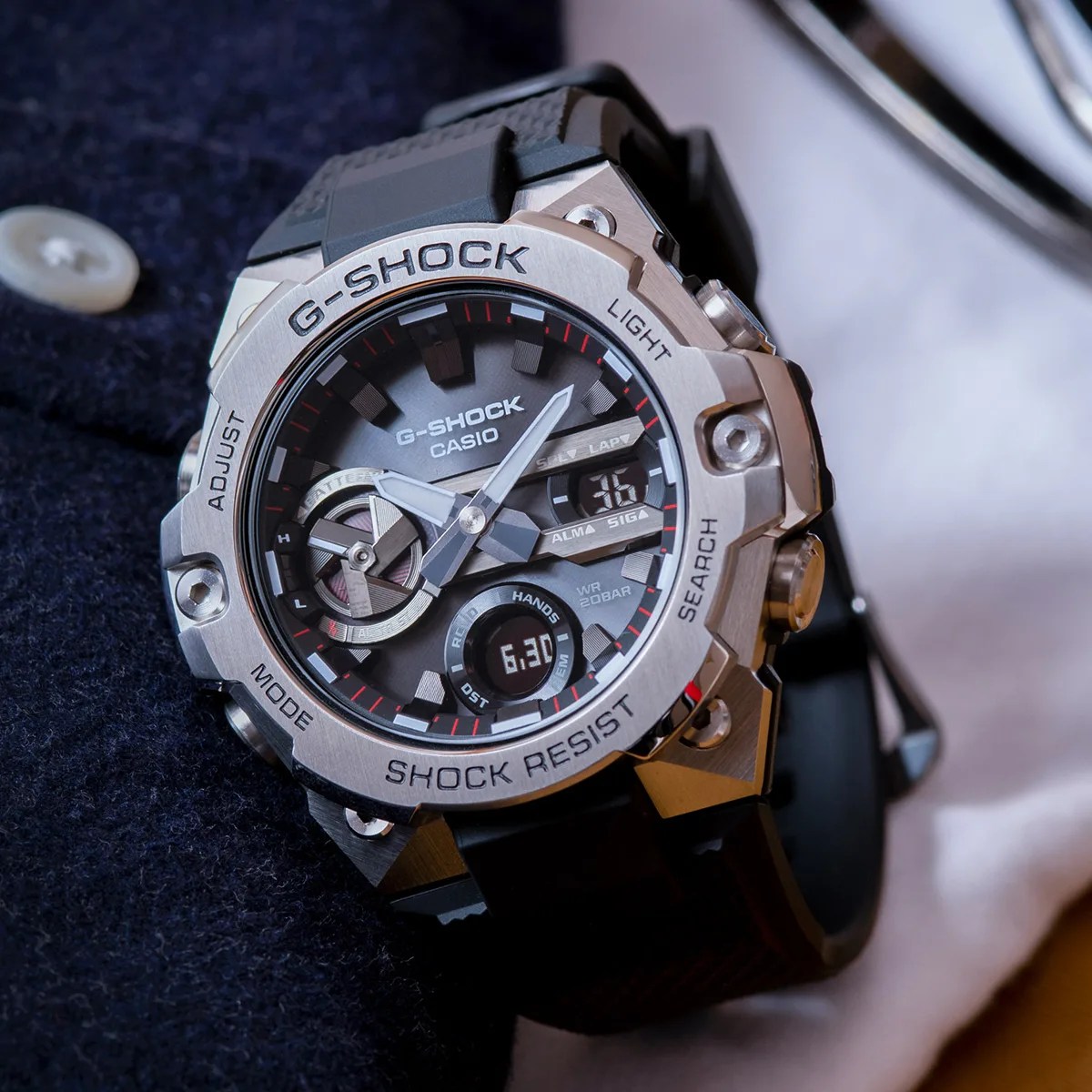 Silver and black Casio G-Shock watch with digital and analog displays on a dark fabric surface.