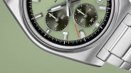 Close-up of a silver stainless steel watch with a green dial, black subdials, and an orange-tipped second hand.