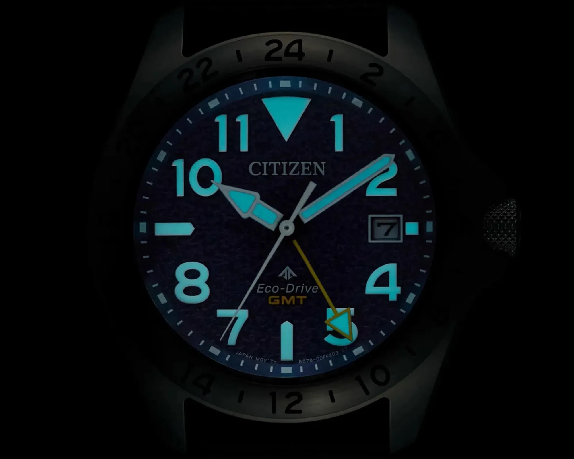 Citizen Eco-Drive GMT watch face glowing blue in the dark with luminescent hands and markers.