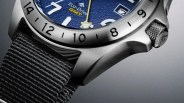 Close-up of a stainless steel watch case with a blue textured dial, black nylon strap, and knurled crown.
