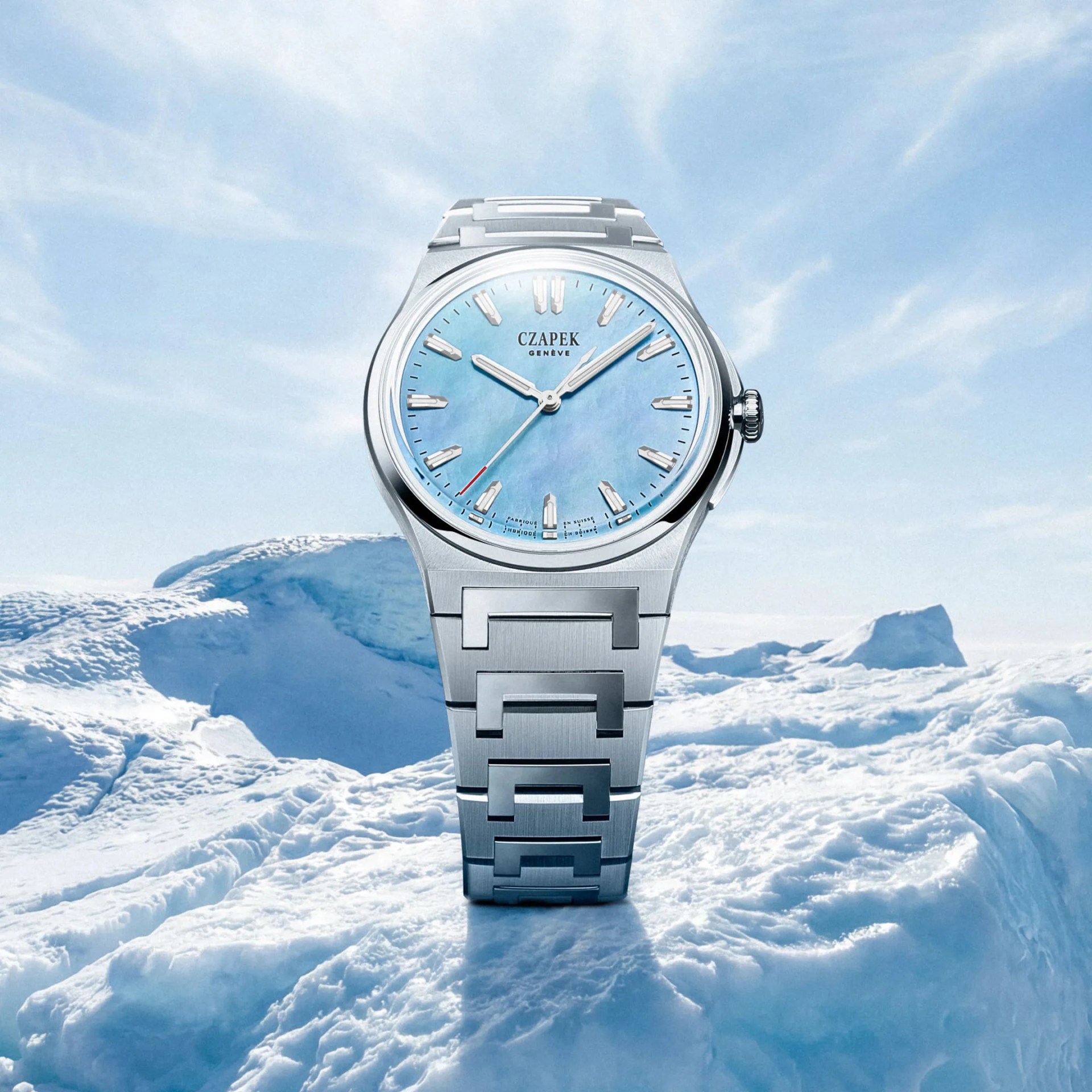 Silver metal wristwatch with a light blue dial and geometric bracelet links on ice.