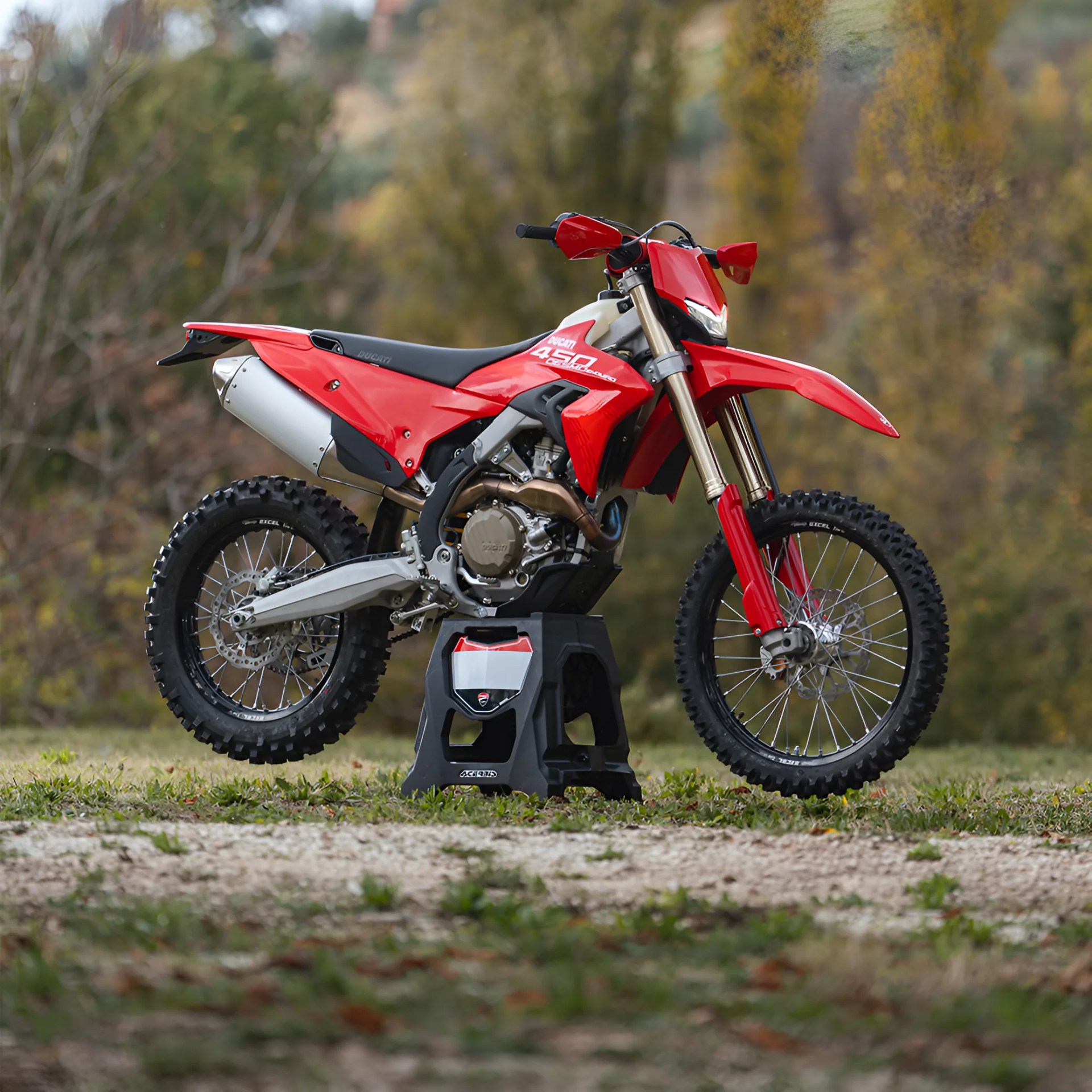 Red Ducati 450 motocross bike on a black stand outdoors with knobby tires and a silver exhaust.