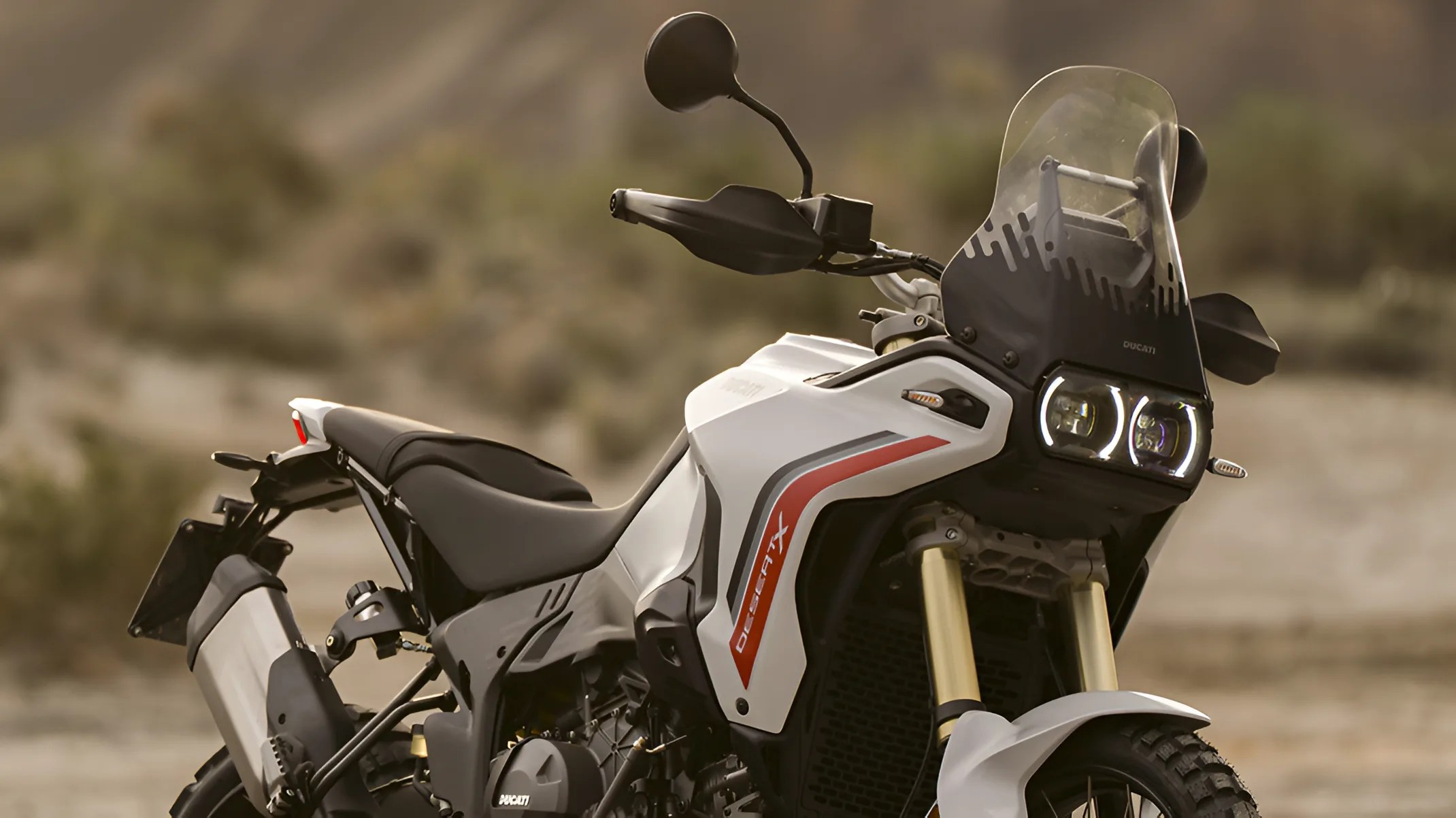 White Ducati DesertX adventure motorcycle with dual round LED headlights and tall windscreen.