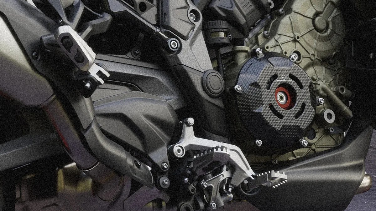 Close-up of a motorcycle engine area showing a carbon fiber cover, foot peg, and metal frame components.
