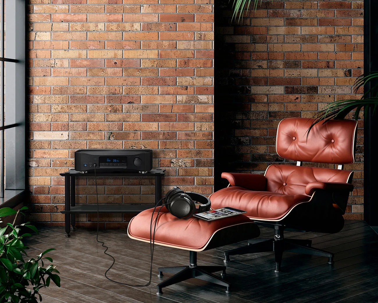 Brown leather lounge chair with matching ottoman, black headphones, and tablet on ottoman in front of brick wall.