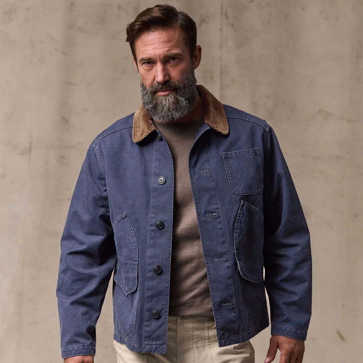 Man wearing a navy blue jacket with a brown corduroy collar over a brown shirt and beige pants.