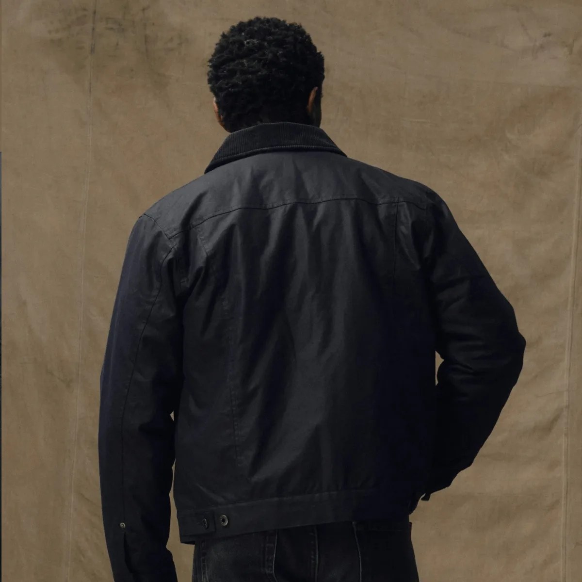 Black jacket with a corduroy collar worn by a person facing away against a beige background.