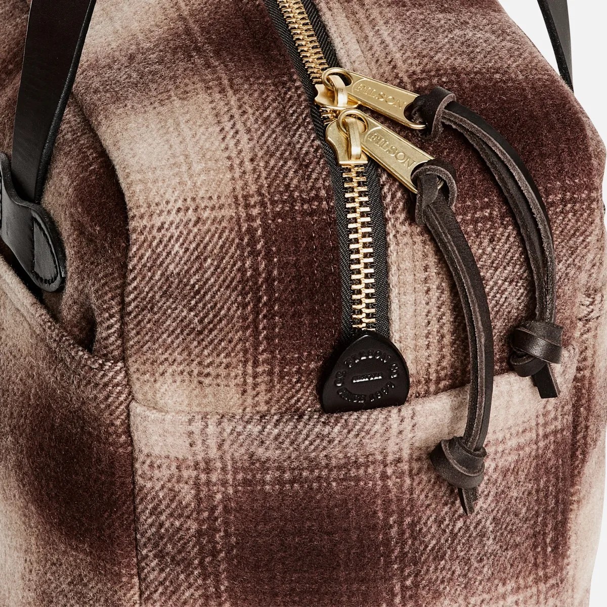 Close-up of a brown and beige plaid fabric bag with gold zippers and black leather zipper pulls.