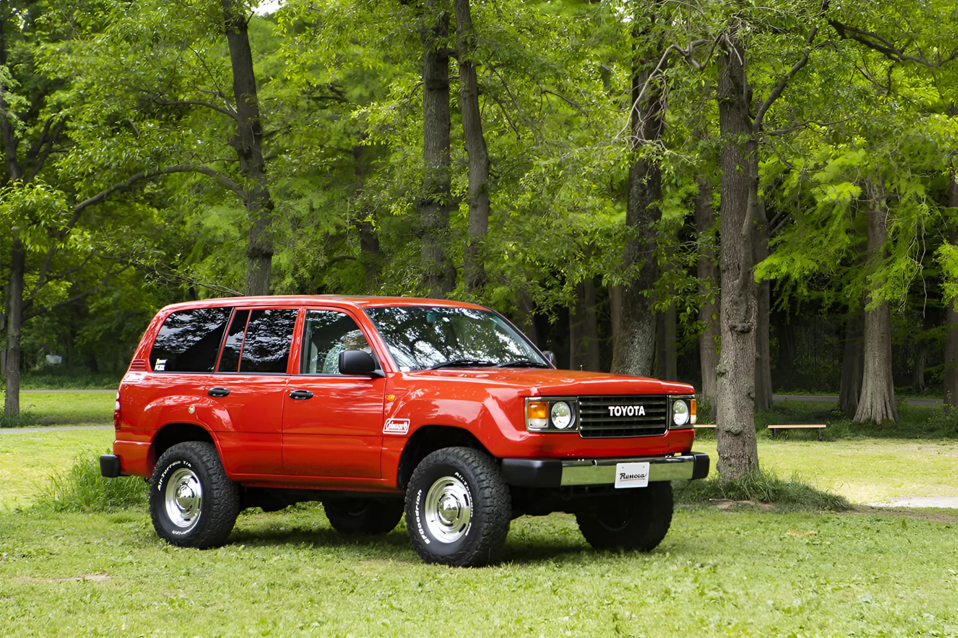 Red Toyota Land Cruiser SUV with black trim and off-road tires parked on grass near trees.