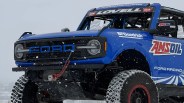 Blue Ford off-road racing truck with large BFGoodrich tires and AMSOIL branding in falling snow.