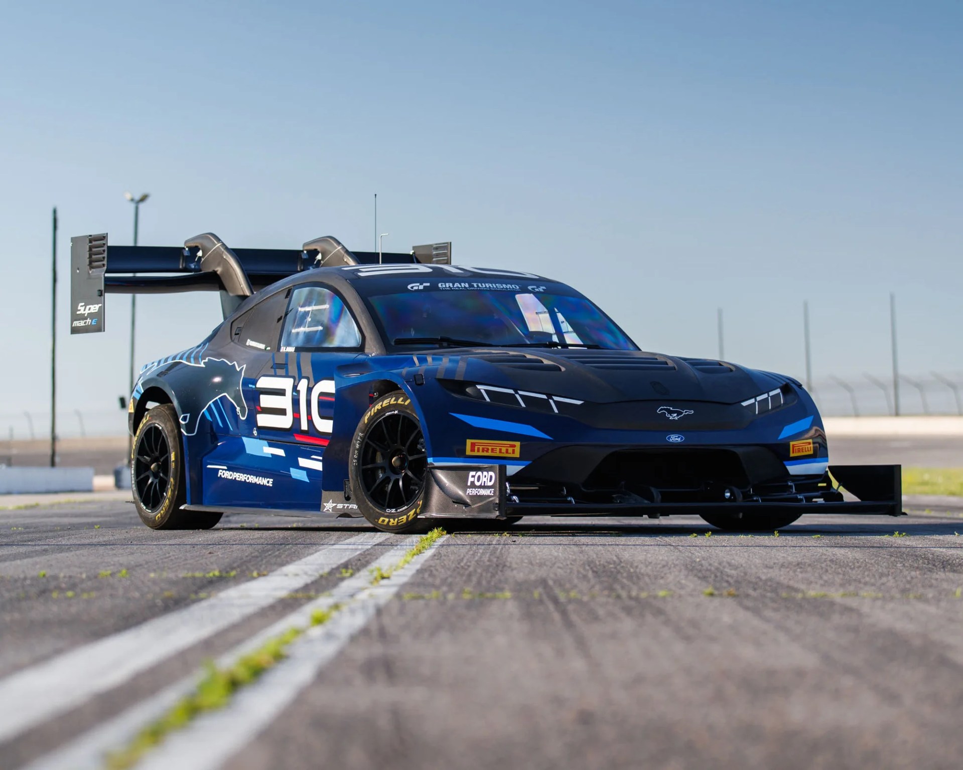 Blue and black Ford Mustang race car with large rear wing and Pirelli tires on a racetrack.