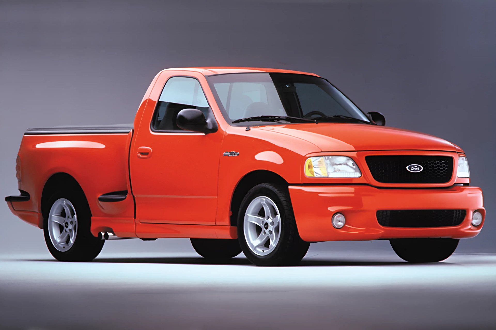 Bright orange Ford pickup truck with black grille and silver alloy wheels on a gray background.