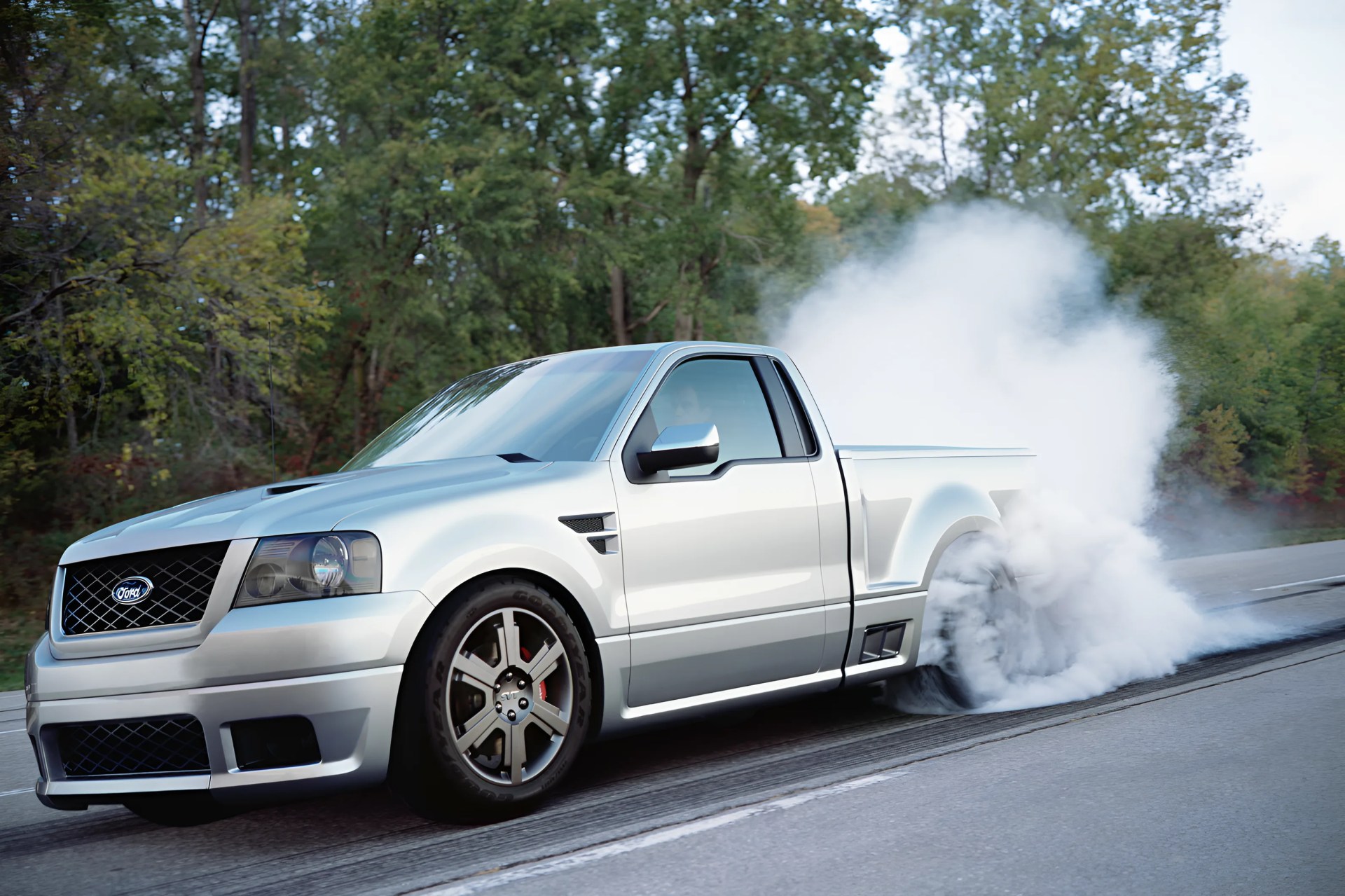 Silver Ford pickup truck performing a burnout on a road with smoke billowing from the rear tires.